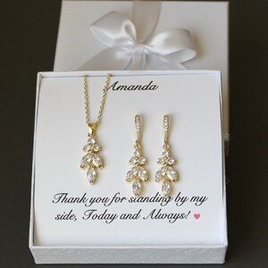 May include: A white gift box with a white satin ribbon bow. The box contains a gold necklace and earrings with clear crystal stones. The box has a message that reads "Thank you for standing by my side, Today and Always!"