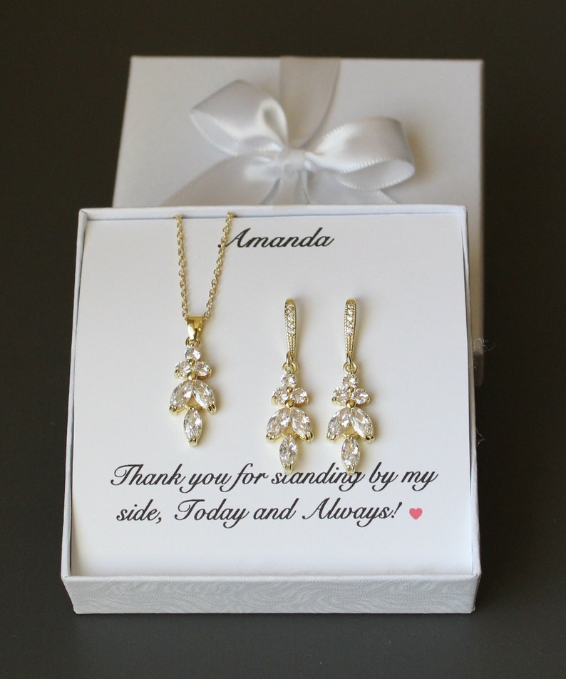 May include: A white gift box with a white satin ribbon bow. The box contains a gold necklace and earrings with clear crystal stones. The box has a message that reads "Thank you for standing by my side, Today and Always!"