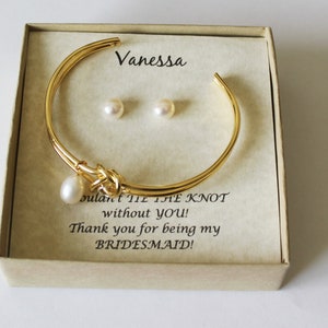 Peut inclure: Un bracelet jonc en or avec un charme en perle et une paire de boucles d'oreilles en perles dans un coffret cadeau. La boîte contient une carte qui dit "Vanessa, je n'aurais pas pu faire le nœud sans toi ! Merci d'être ma demoiselle d'honneur !"