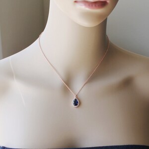 May include: A rose gold necklace with a teardrop-shaped pendant featuring a dark blue sapphire surrounded by a halo of smaller clear stones.