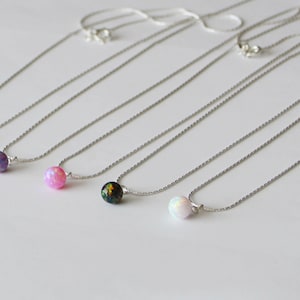 May include: Five silver necklaces with different colored opal stones. The stones are orange, purple, pink, black, and white.