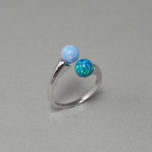 May include: A silver ring with two opal stones. One stone is light blue and the other is a darker blue-green.