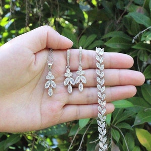 May include: A silver necklace, earrings, and bracelet set with clear crystal stones in a leaf design.