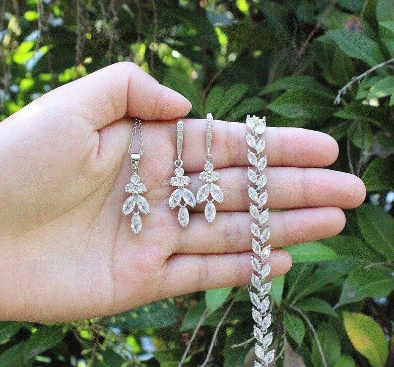 May include: A silver necklace, earrings, and bracelet set with clear crystal stones in a leaf design.