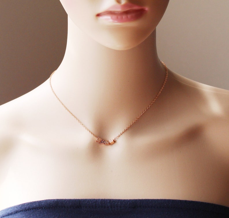 Puede incluir: Un collar de cadena dorada con un colgante que deletrea "LOVE" en letras peque&ntilde;as y c&uacute;bicas.