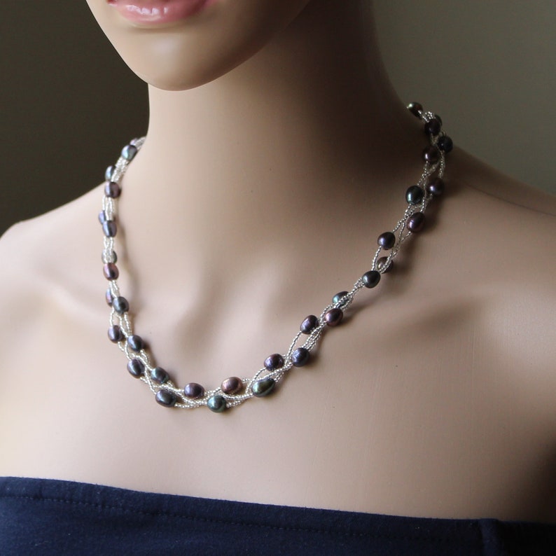 Op de afbeelding: Een zilveren en zwarte parelketting met een gevlochten ontwerp. De ketting is gemaakt van kleine, ronde parels die in een gevlochten patroon aan elkaar geregen zijn. De parels zijn een mix van zwart en zilver, en de ketting is ongeveer 46 cm lang.