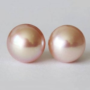 May include: A pair of round, smooth, light pink pearls with a lustrous, reflective surface. Each pearl exhibits a soft, iridescent sheen and a uniform spherical shape, showcasing a delicate pastel color palette and a polished, high-gloss finish.