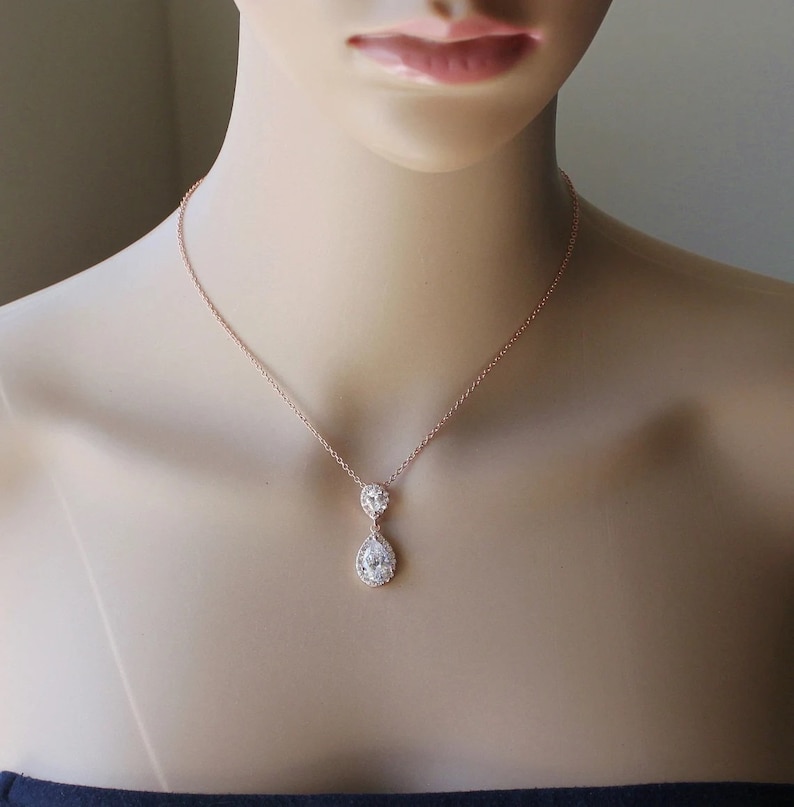 May include: A rose gold necklace with a teardrop-shaped pendant featuring two clear cubic zirconia stones.