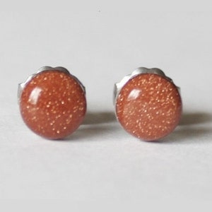 May include: A pair of silver stud earrings with round, orange-brown sandstone stones.