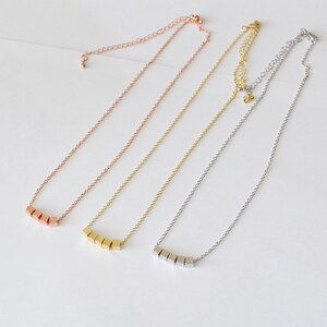 Puede incluir: Tres delicados collares con una cadena y una fila de peque&ntilde;os colgantes cuadrados. Los collares son de oro rosa, oro y plata.