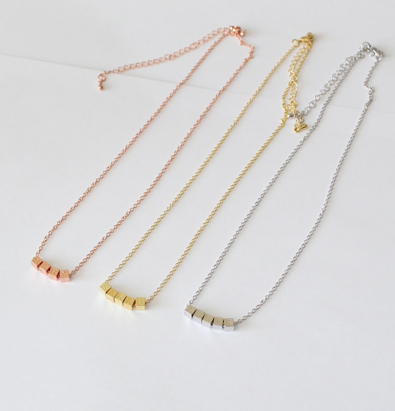 Puede incluir: Tres delicados collares con una cadena y una fila de peque&ntilde;os colgantes cuadrados. Los collares son de oro rosa, oro y plata.