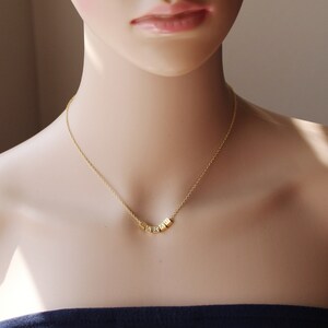 Puede incluir: Un collar de cadena dorada con un colgante que deletrea la palabra "LOVE" en letras de bloque.