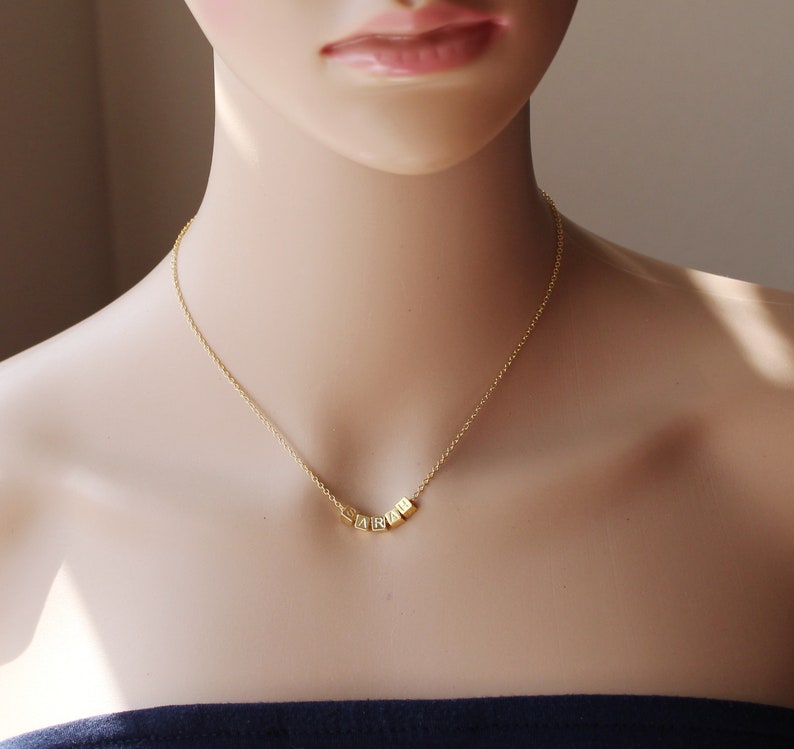 Puede incluir: Un collar de cadena dorada con un colgante que deletrea la palabra "LOVE" en letras de bloque.