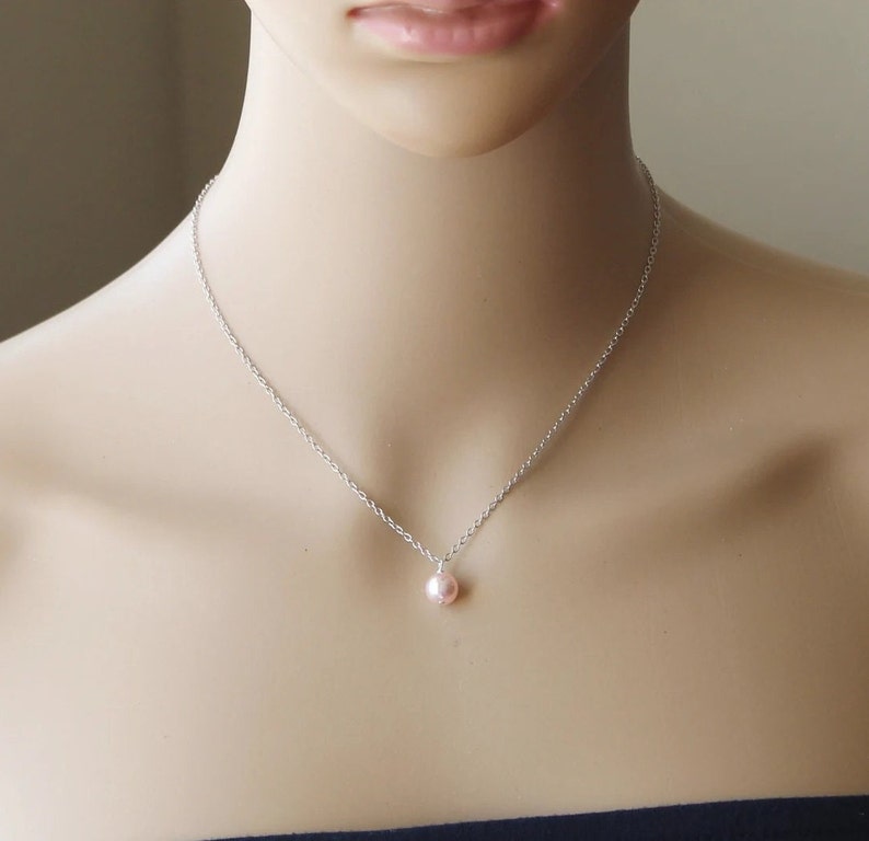 May include: A delicate silver chain necklace with a single pink pearl pendant.
