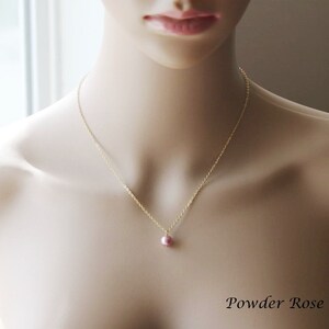 May include: A delicate gold chain necklace with a single small pink pearl pendant. The necklace is displayed on a mannequin.