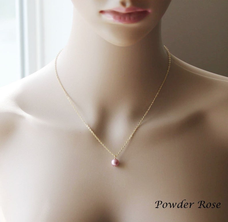 May include: A delicate gold chain necklace with a single small pink pearl pendant. The necklace is displayed on a mannequin.