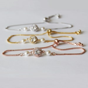 May include: Three adjustable bracelets with a silver, gold, and rose gold chain. Each bracelet features a round crystal with a halo of smaller crystals and two white pearls.