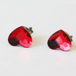 May include: A pair of red heart-shaped stud earrings. The earrings are made of metal and have a clear crystal in the centre.