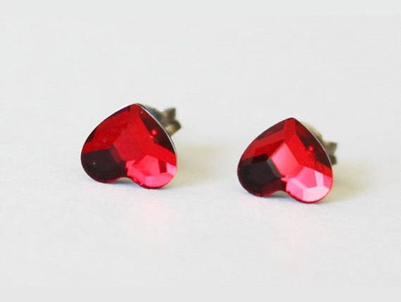 May include: A pair of red heart-shaped stud earrings. The earrings are made of metal and have a clear crystal in the centre.