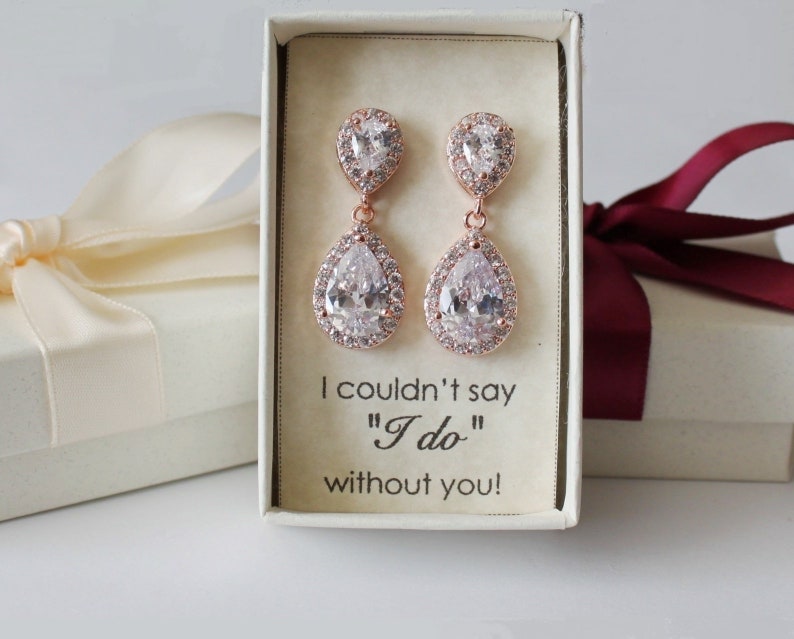 May include: Rose gold teardrop earrings with clear cubic zirconia stones. The earrings are in a small white box with the text "I couldn't say "I do" without you!"