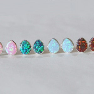 May include: A set of eight teardrop-shaped opal earrings in various colors, including pink, blue, green, white, and red. The earrings are set in silver.