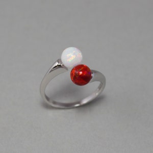 May include: A silver ring with two round opals, one white and one red.
