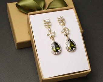 May include: A pair of gold-tone drop earrings featuring a leaf-shaped design with clear crystals and a large olive green teardrop-shaped stone at the base, presented in a tan gift box with a green ribbon. The text color # 6 is visible.