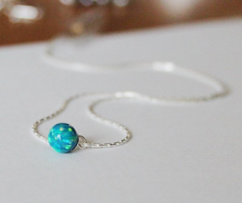 May include: A delicate silver chain necklace with a single round blue opal pendant.
