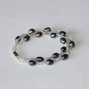 Op de afbeelding: Een meerstrengs armband met donkergrijze ovale parels en zilveren kralen.