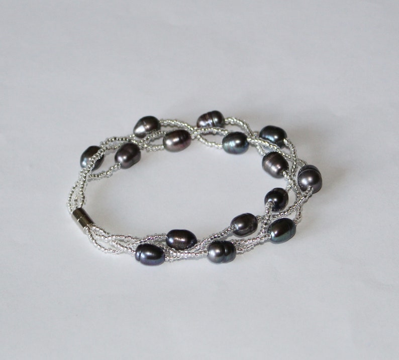Op de afbeelding: Een meerstrengs armband met donkergrijze ovale parels en zilveren kralen.