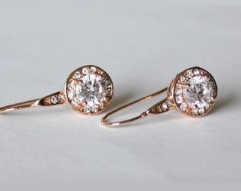 May include: A pair of rose gold dangle earrings with a large round clear crystal surrounded by smaller crystals.