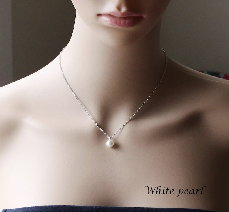 May include: A simple silver chain necklace with a single white pearl pendant. The necklace is on a mannequin's neck. "White pearl" is written in the bottom right corner of the image.