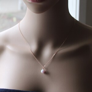May include: A delicate rose gold chain necklace with a small pink opal pendant.