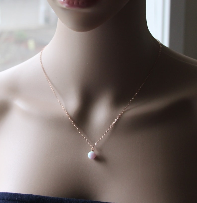 May include: A delicate rose gold chain necklace with a small pink opal pendant.