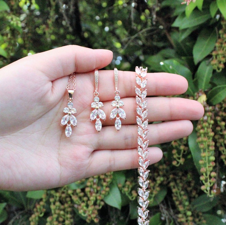 May include: A rose gold bridal jewelry set with a necklace, earrings, and bracelet. The set features a delicate floral design with clear cubic zirconia stones.