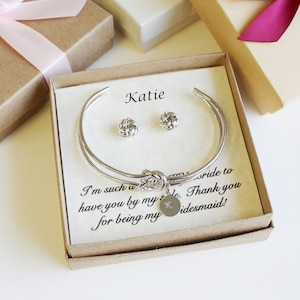 May include: A gift box containing a silver bracelet and earrings. The box has a card inside that reads "Katie I'm such a ... have you by my side. Thank you for being my bridesmaid!"
