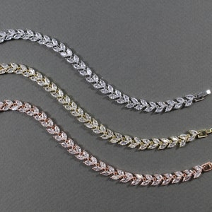 May include: Three delicate bracelets with a leaf design, each with a different metal finish: silver, gold, and rose gold. The bracelets are made of small, clear cubic zirconia stones set in a leaf shape.