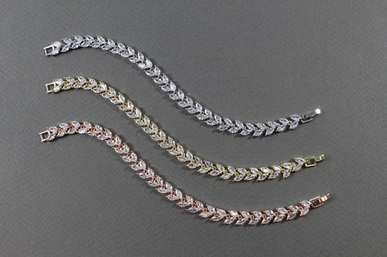 May include: Three delicate bracelets with a leaf design, each with a different metal finish: silver, gold, and rose gold. The bracelets are made of small, clear cubic zirconia stones set in a leaf shape.