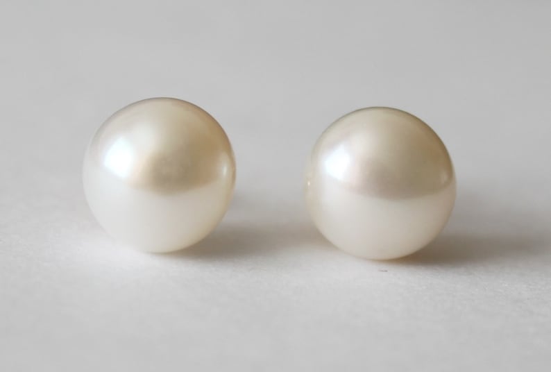Puede incluir: Un par de pendientes de perlas blancas. Las perlas son redondas y lisas.