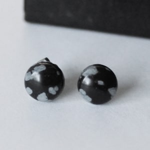 May include: A pair of black and white snowflake obsidian stud earrings. The earrings are round and have a silver backing.