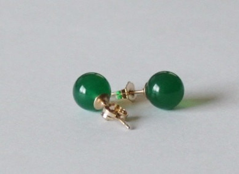 May include: A pair of green gemstone stud earrings with gold posts.