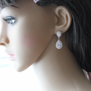 May include: Silver teardrop earrings with a large clear crystal surrounded by smaller crystals.