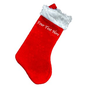 May include: A red Christmas stocking with a white faux fur trim. The stocking features the text "Your Text Here" in white script. The stocking is angled to the left against a white backdrop.