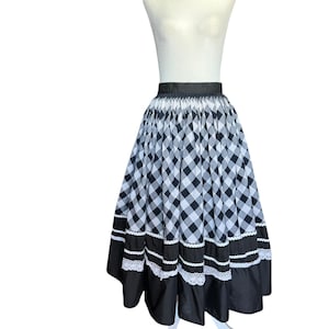 May include: A black and white checkered skirt with a black waistband and hem. The skirt has a full, pleated design with white lace trim. The skirt is displayed on a white mannequin.
