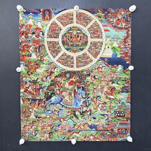 May include: A vibrant Buddhist thangka painting showing the Wheel of Life. The artwork is filled with figures, animals, and scenes within a circular design, with a central figure and a mountain landscape. The colour palette includes reds, blues, greens, and yellows.