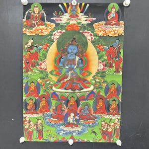 May include: A vibrant religious poster depicting a central blue deity surrounded by smaller figures in various poses. The artwork incorporates floral and geometric patterns, with a dominant green and red colour scheme. The poster is held in place by white drawing pins.