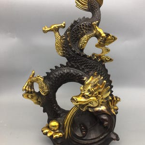 May include: A bronze dragon sculpture with gold accents. The dragon is depicted in a dynamic pose, with its body curving and its head raised. The sculpture has intricate details, including scales and flowing mane.