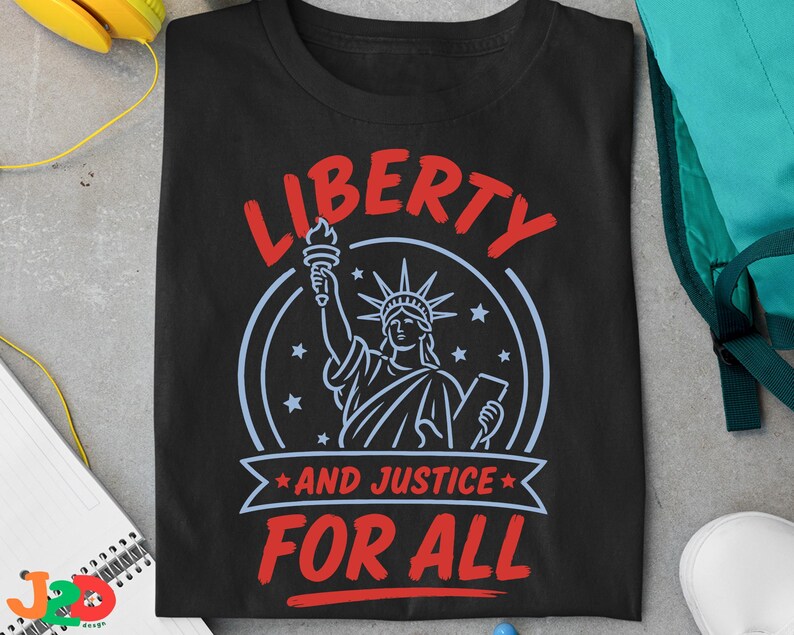 May include: A black t-shirt featuring a graphic of the Statue of Liberty in light blue, surrounded by stars. The text in red reads LIBERTY at the top and AND JUSTICE FOR ALL on a banner below the statue, with a circular border surrounding the design.