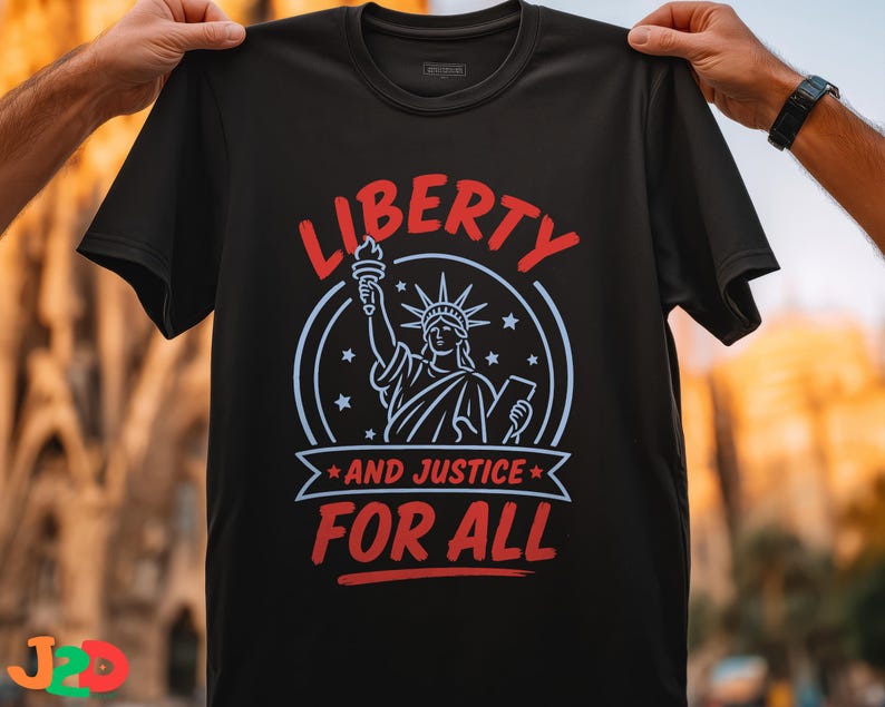 May include: A black short-sleeved t-shirt featuring a graphic of the Statue of Liberty in light blue lines. The text LIBERTY in red arches above, with AND JUSTICE FOR ALL in red below, all enclosed within a circular frame with small stars.