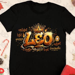 May include: Black t-shirt featuring a gold and orange graphic design with the word "LEO" in a graffiti style. The design includes a crown, constellation, and words like "confident" and "creative".